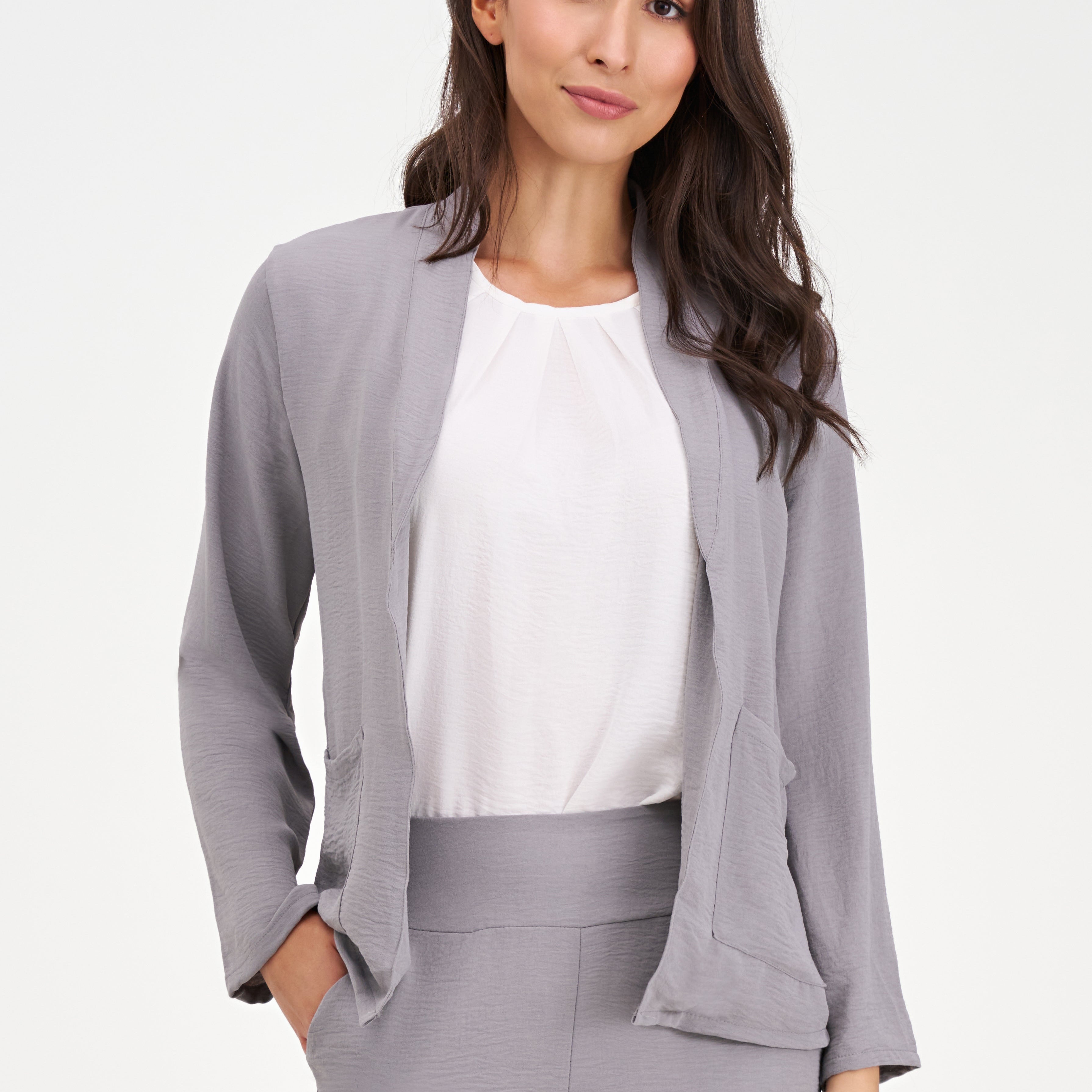 Veste fluide pour femme de couleur gris brouillard, marque M made in Italy. Coupe légère et tombé élégant, conçue en 100% polyester. L'image montre la texture lisse du tissu et la finesse de la confection italienne, idéale pour un look sophistiqué et aérien.