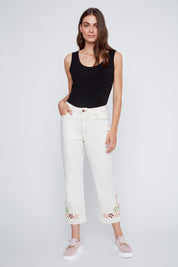 Jeans écru avec coutures beige contrastées et broderies de fleurs au bas des jambes, style féminin et estival.