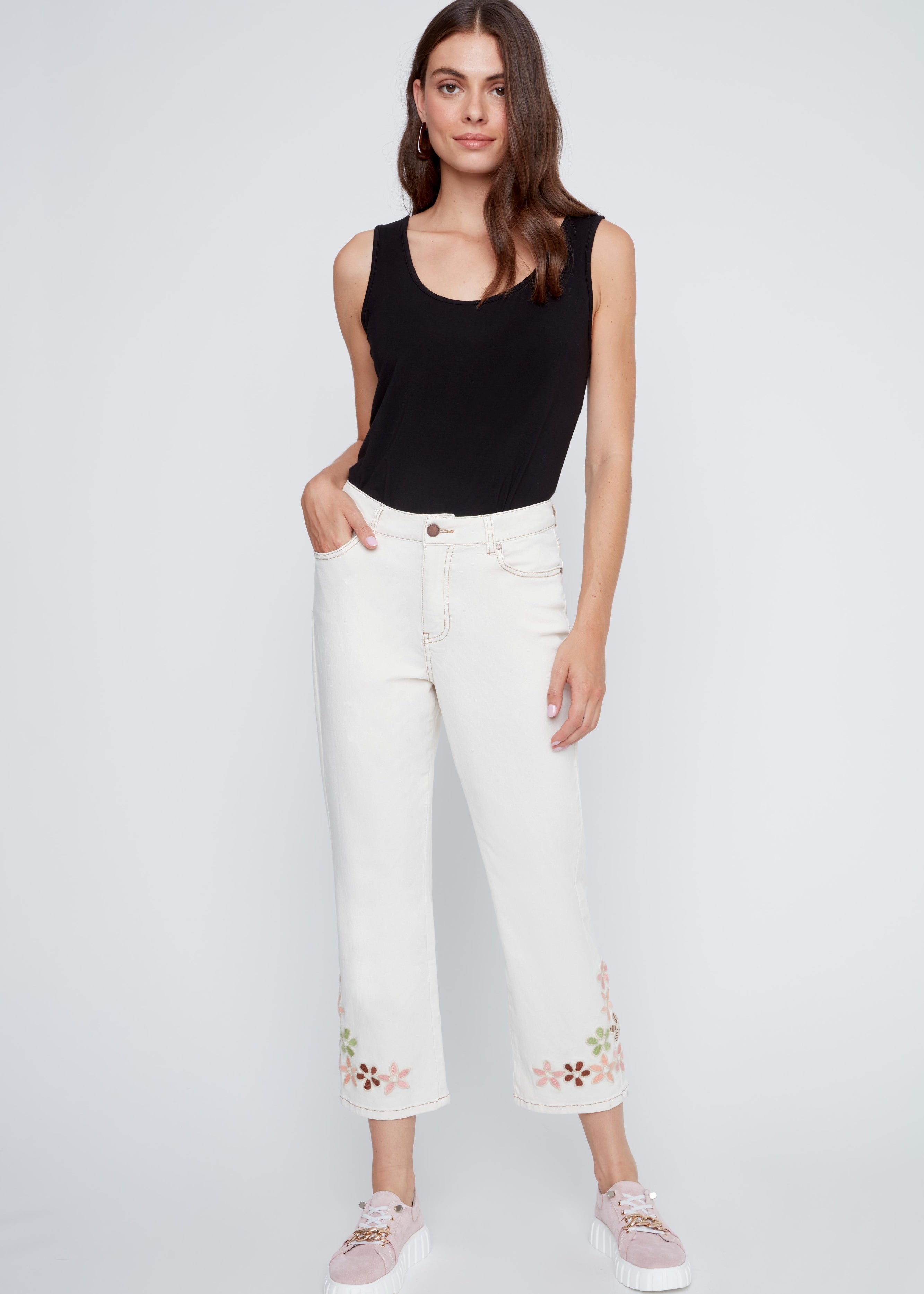 Jeans écru avec coutures beige contrastées et broderies de fleurs au bas des jambes, style féminin et estival.