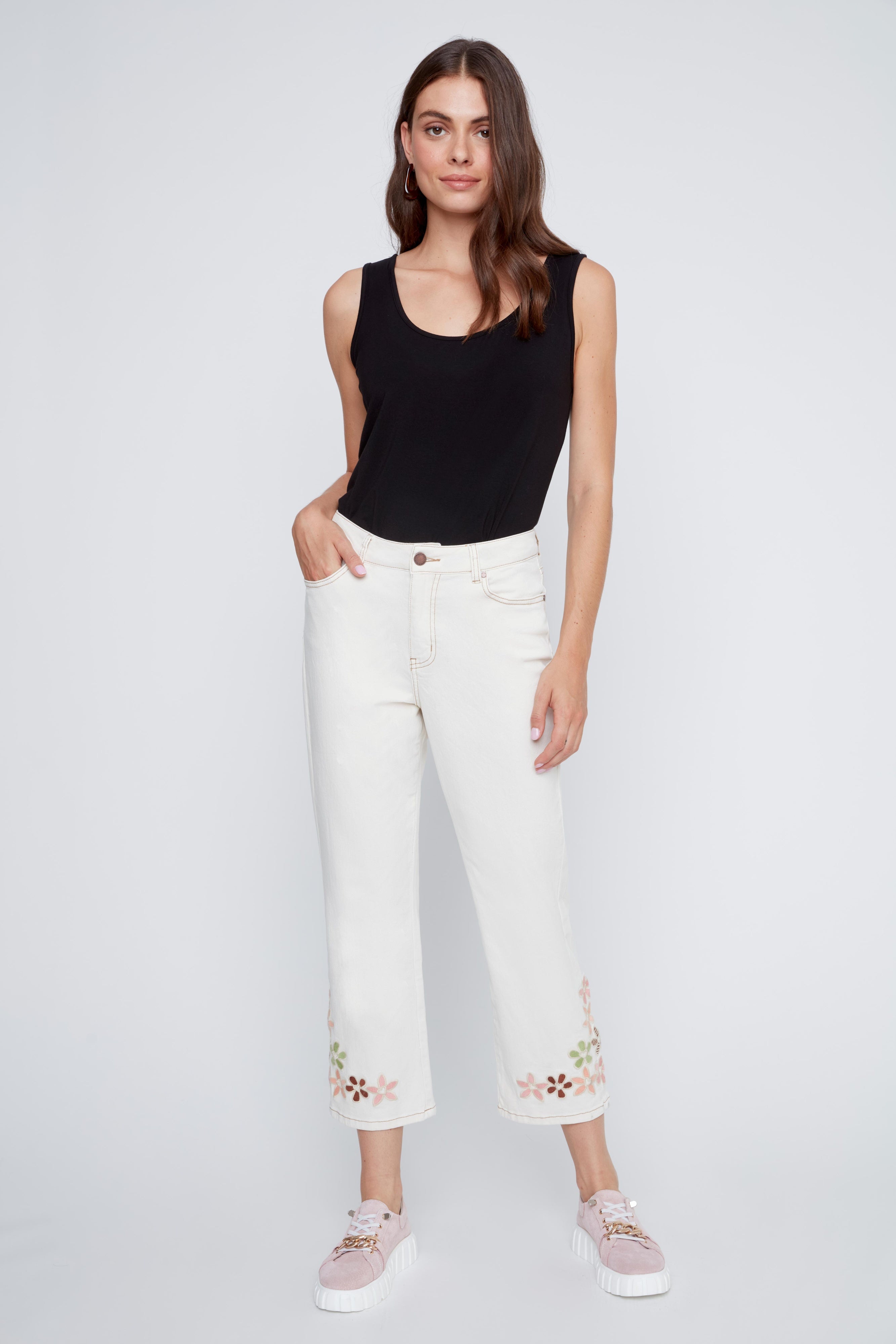 Jeans écru avec coutures beige contrastées et broderies de fleurs au bas des jambes, style féminin et estival.
