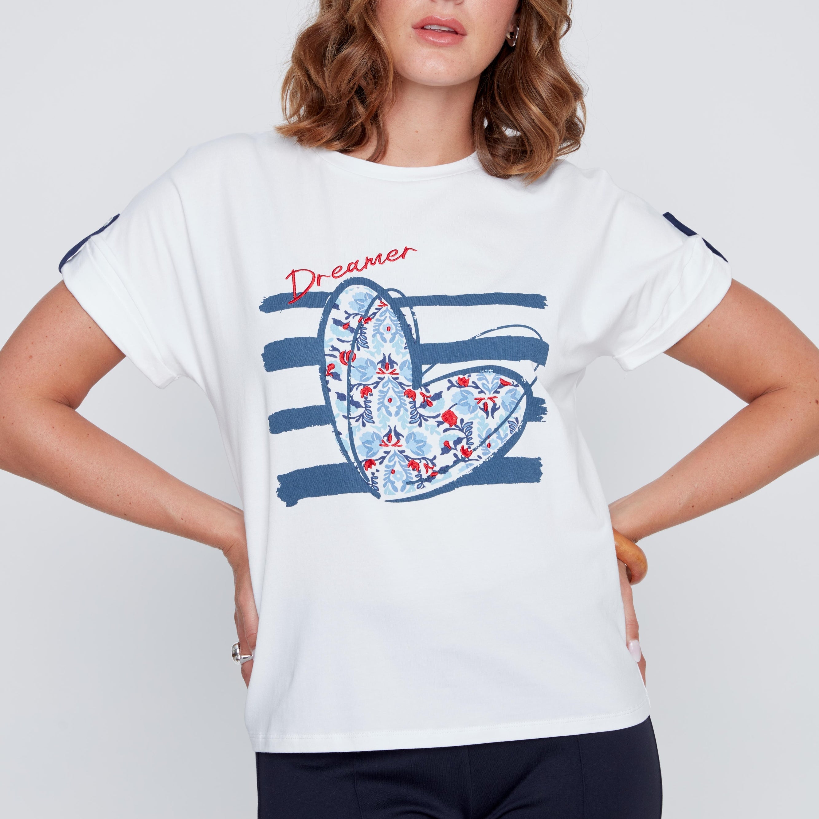 T-shirt blanc à col rond avec imprimé cœur aux tons de bleu, petits détails brodés et inscription Dreamer rouge, léger détail marine et petit bouton d’attache.