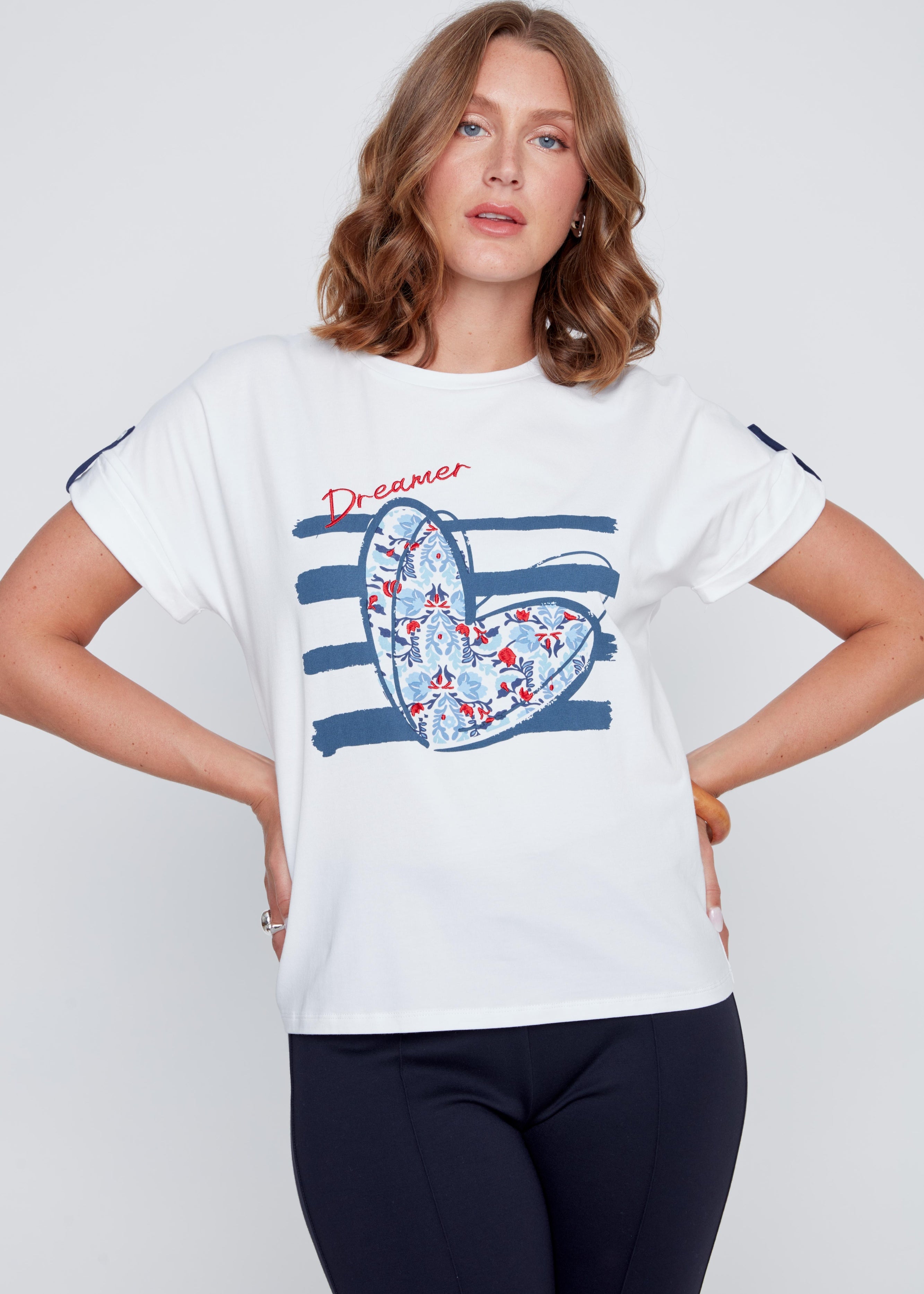 T-shirt blanc à col rond avec imprimé cœur aux tons de bleu, petits détails brodés et inscription Dreamer rouge, léger détail marine et petit bouton d’attache.