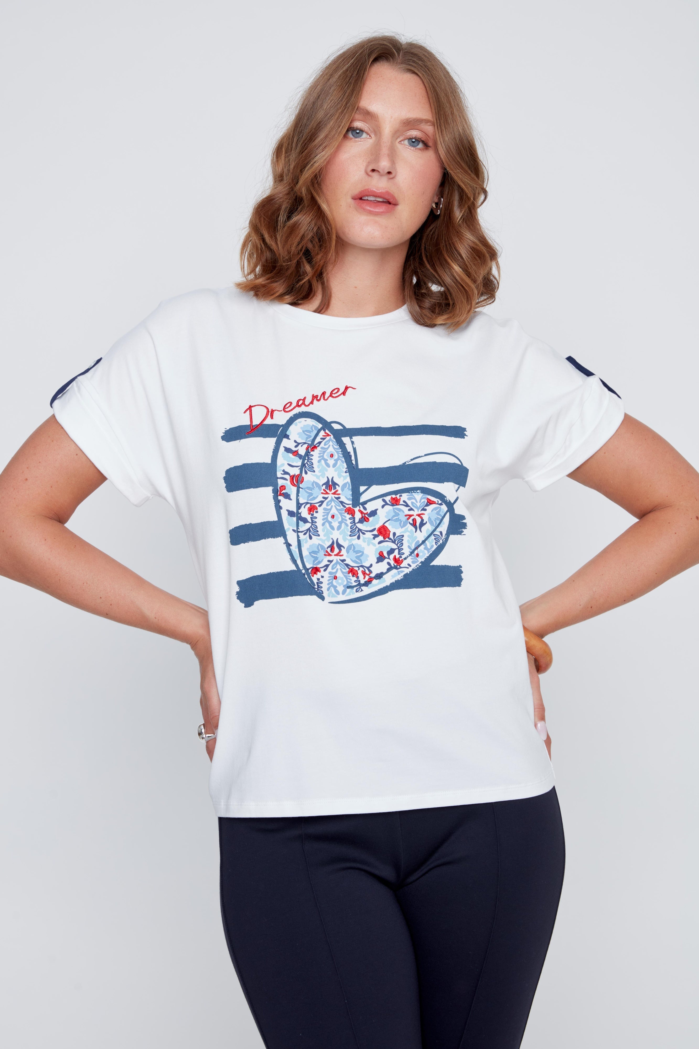 T-shirt blanc à col rond avec imprimé cœur aux tons de bleu, petits détails brodés et inscription Dreamer rouge, léger détail marine et petit bouton d’attache.