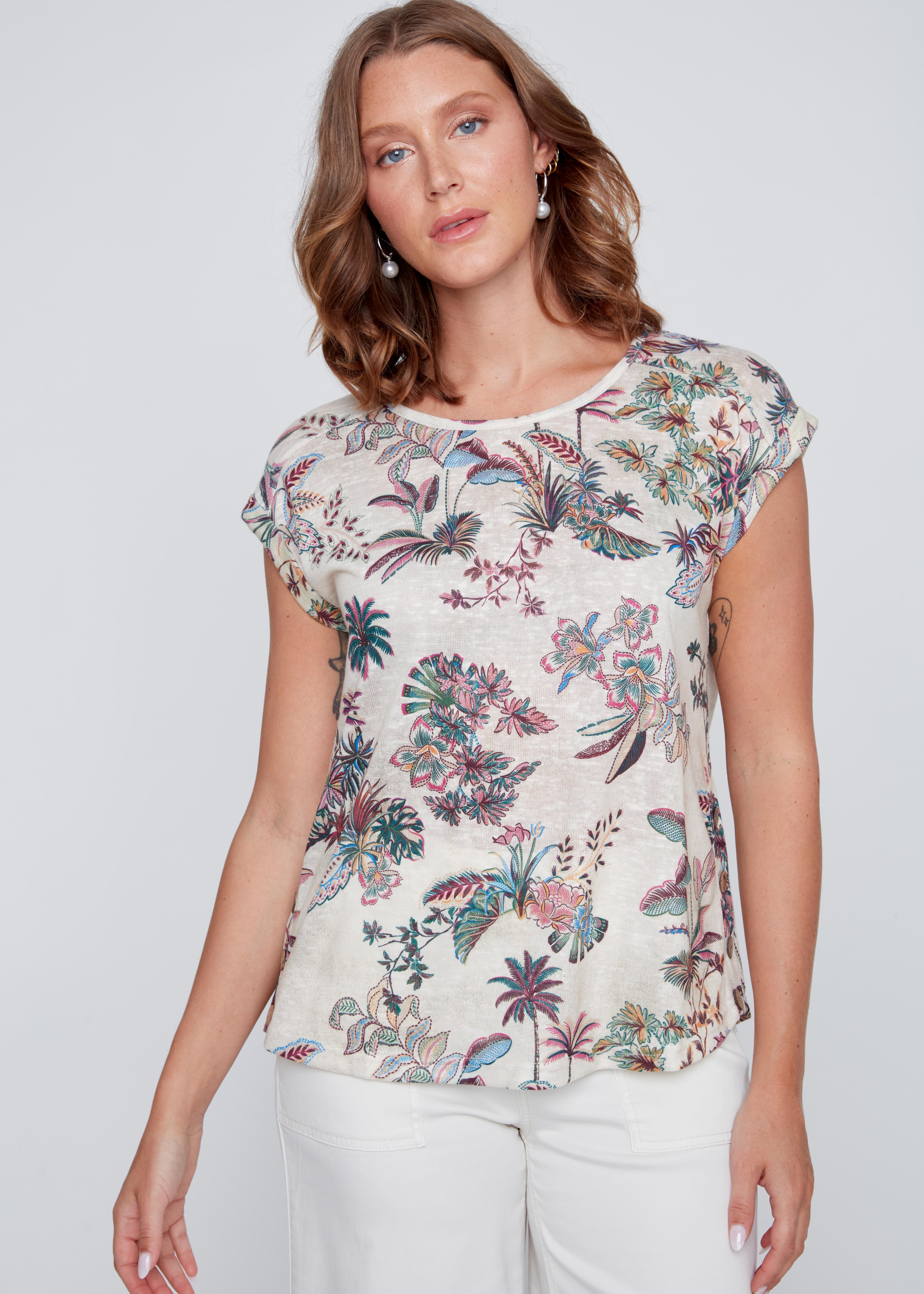 T-shirt écru à col rond avec imprimé tropical rose et vert, boutons décoratifs en bois au bas du chandail près des hanches.