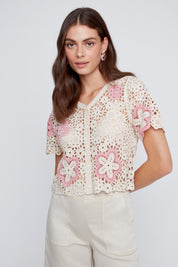 Chandail en crochet écru avec fleurs ajourées et perles à l’avant, dos à motifs de cercles et lignes rose et écru.