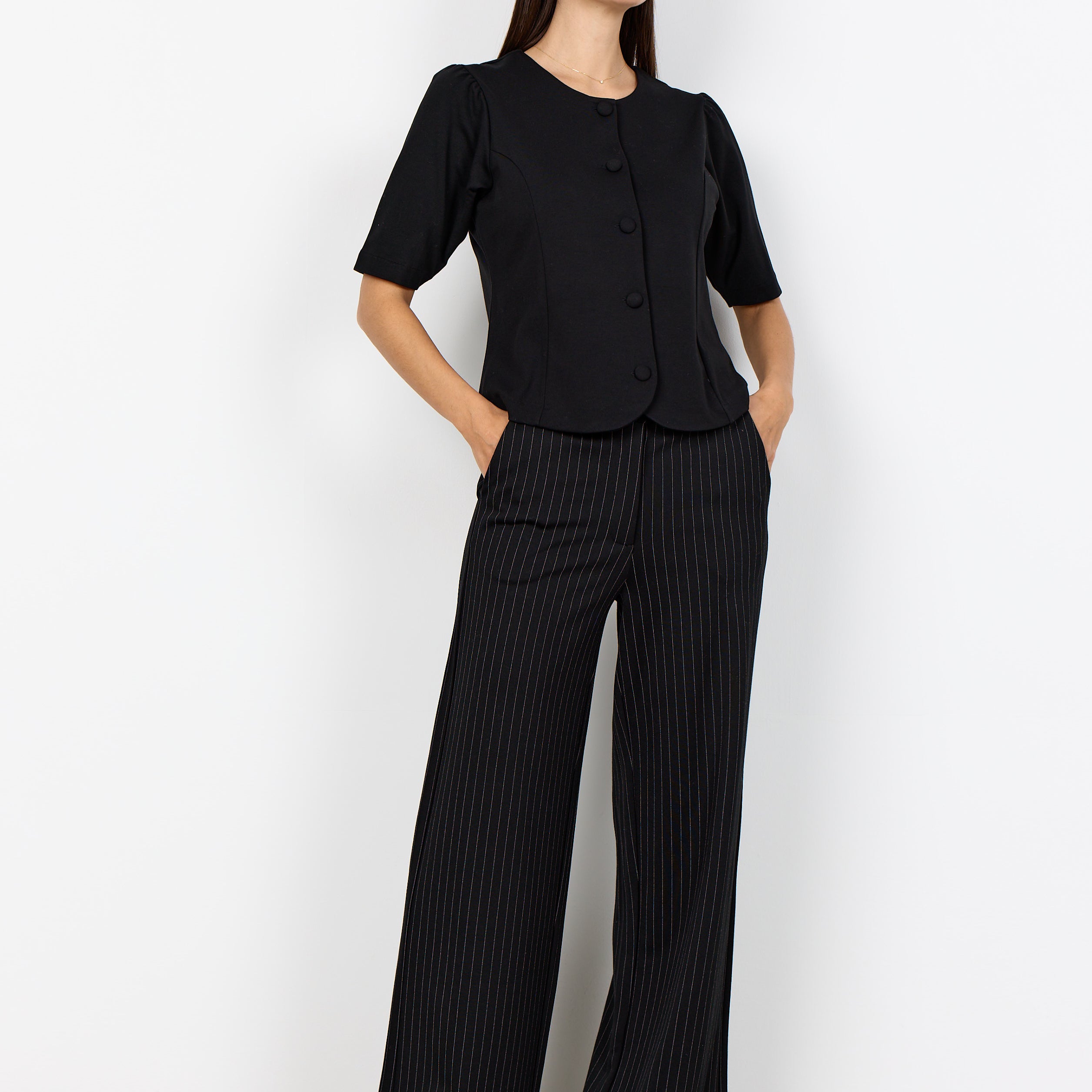 Pantalon noir à fines rayures porté avec un haut uni.