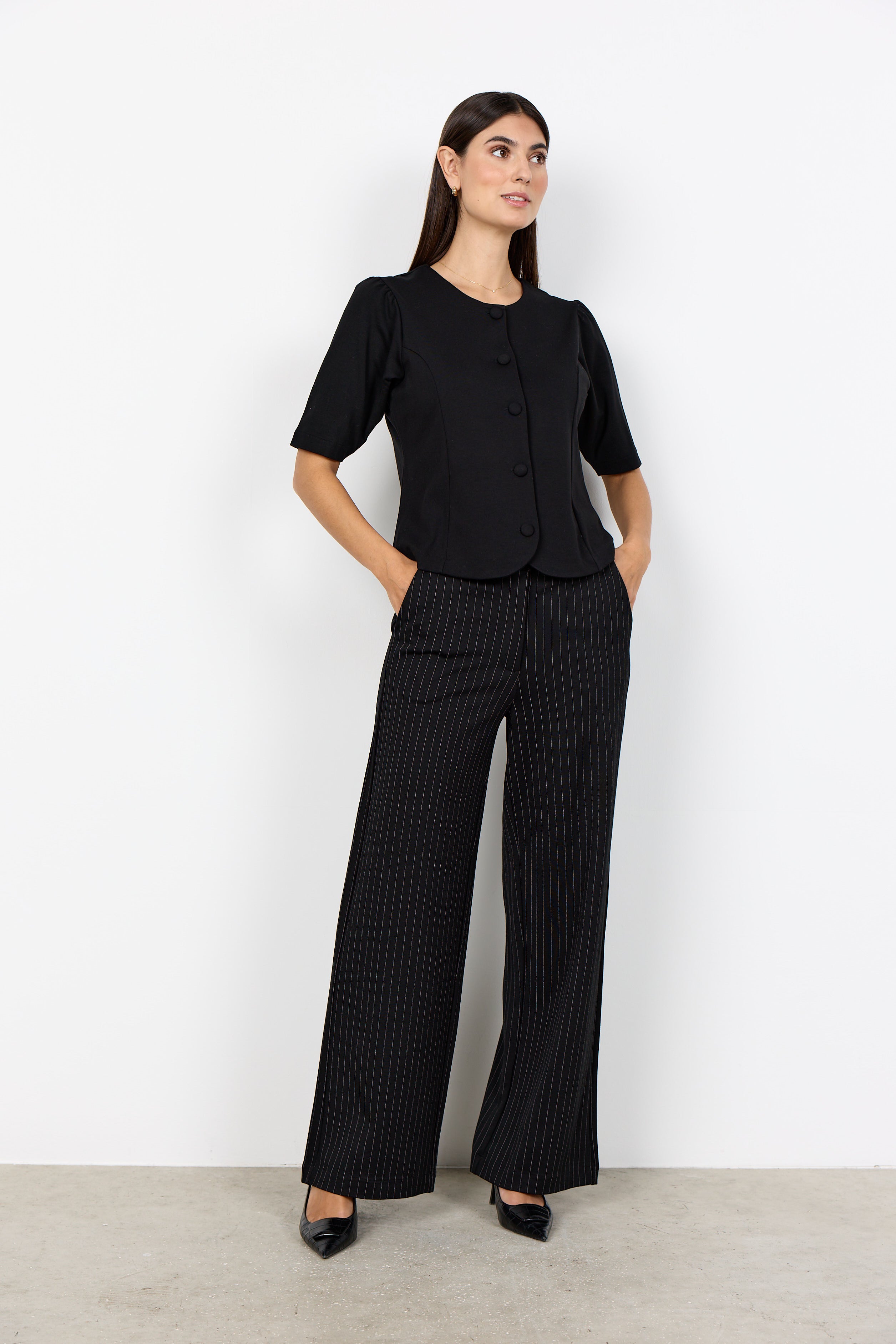 Pantalon noir à fines rayures porté avec un haut uni.