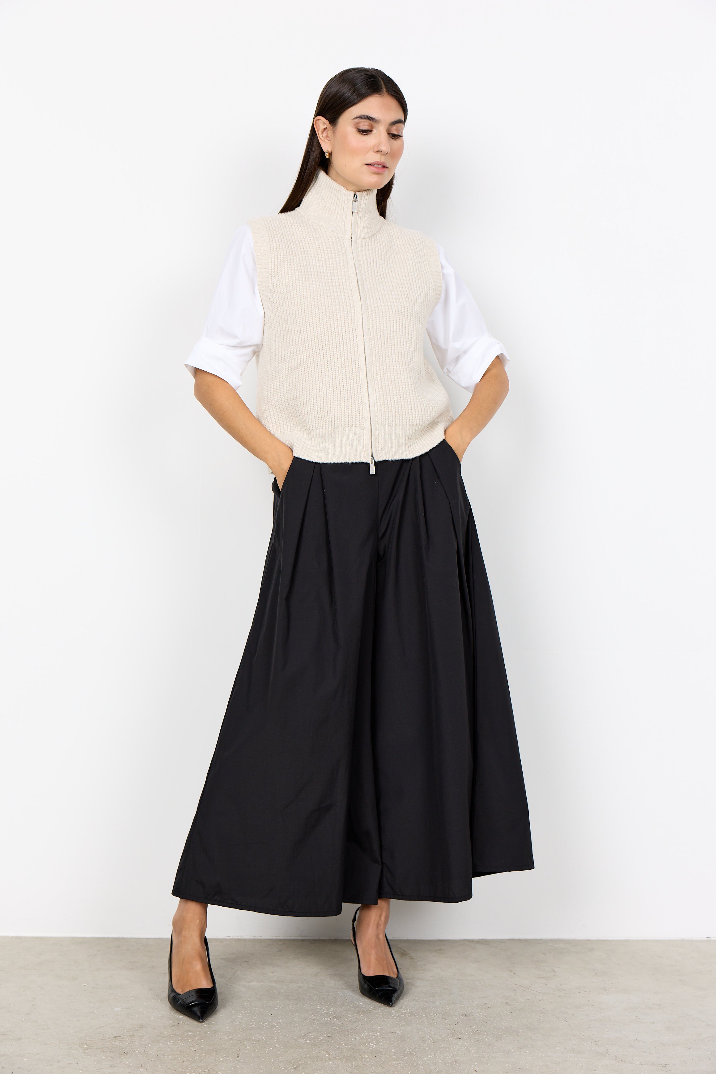 Veste en tricot crème portée sur une blouse blanche avec jupe noire