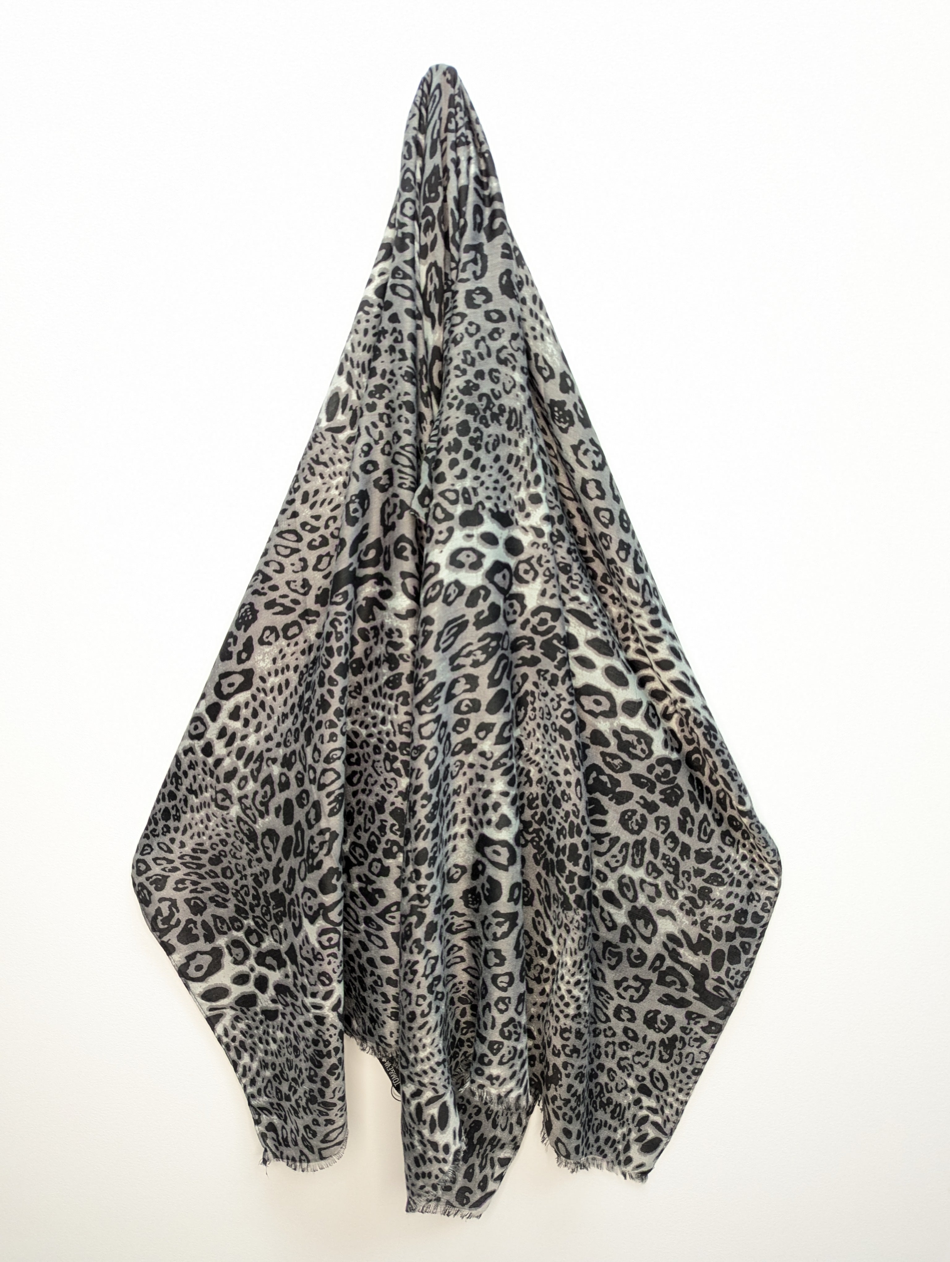 "Foulard ou écharpe à motif léopard dans une palette de gris, de noir. Le tissu est léger et doux, idéal pour ajouter une touche de sophistication à une tenue sobre."