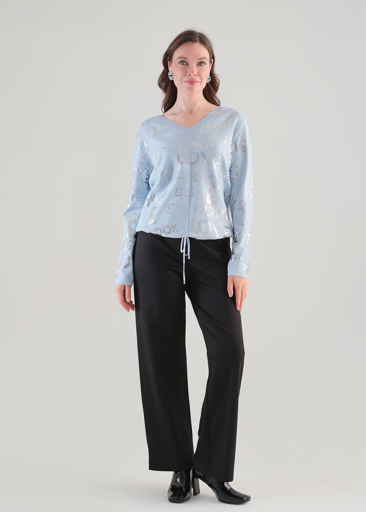 Femme portant le chandail bleu Tricotto 96111 à col V, motif lettré argenté et cordon ajustable, vue de face