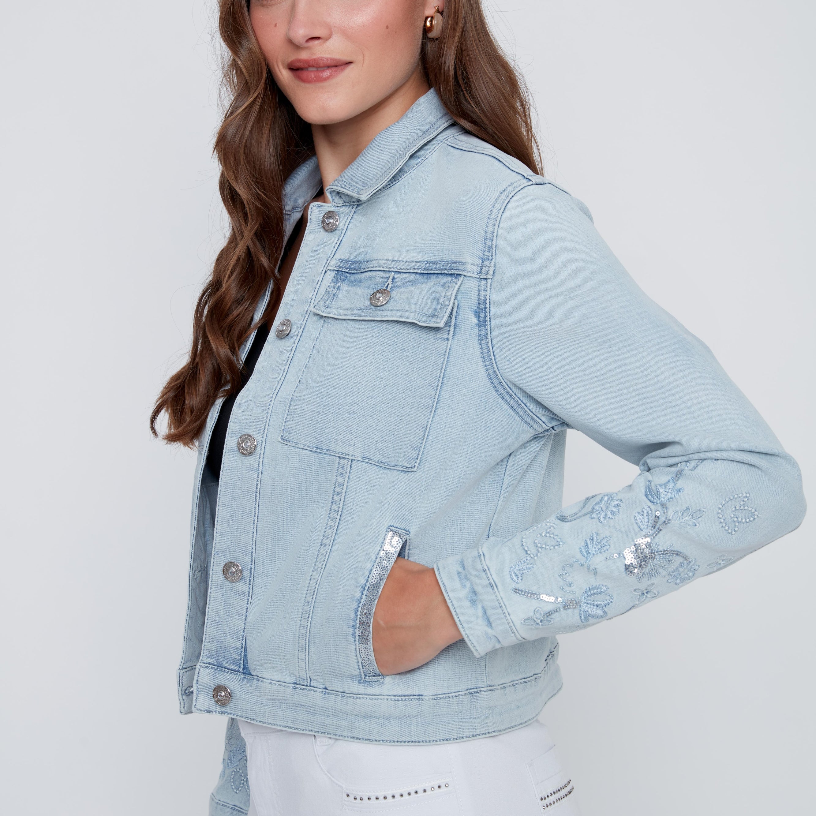 Veste de jeans pour femme en bleu denim pâle avec broderies florales à paillettes, détails brillants aux poches et boutons de fermeture à l’avant.