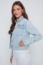 Veste de jeans pour femme en bleu denim pâle avec broderies florales à paillettes, détails brillants aux poches et boutons de fermeture à l’avant.