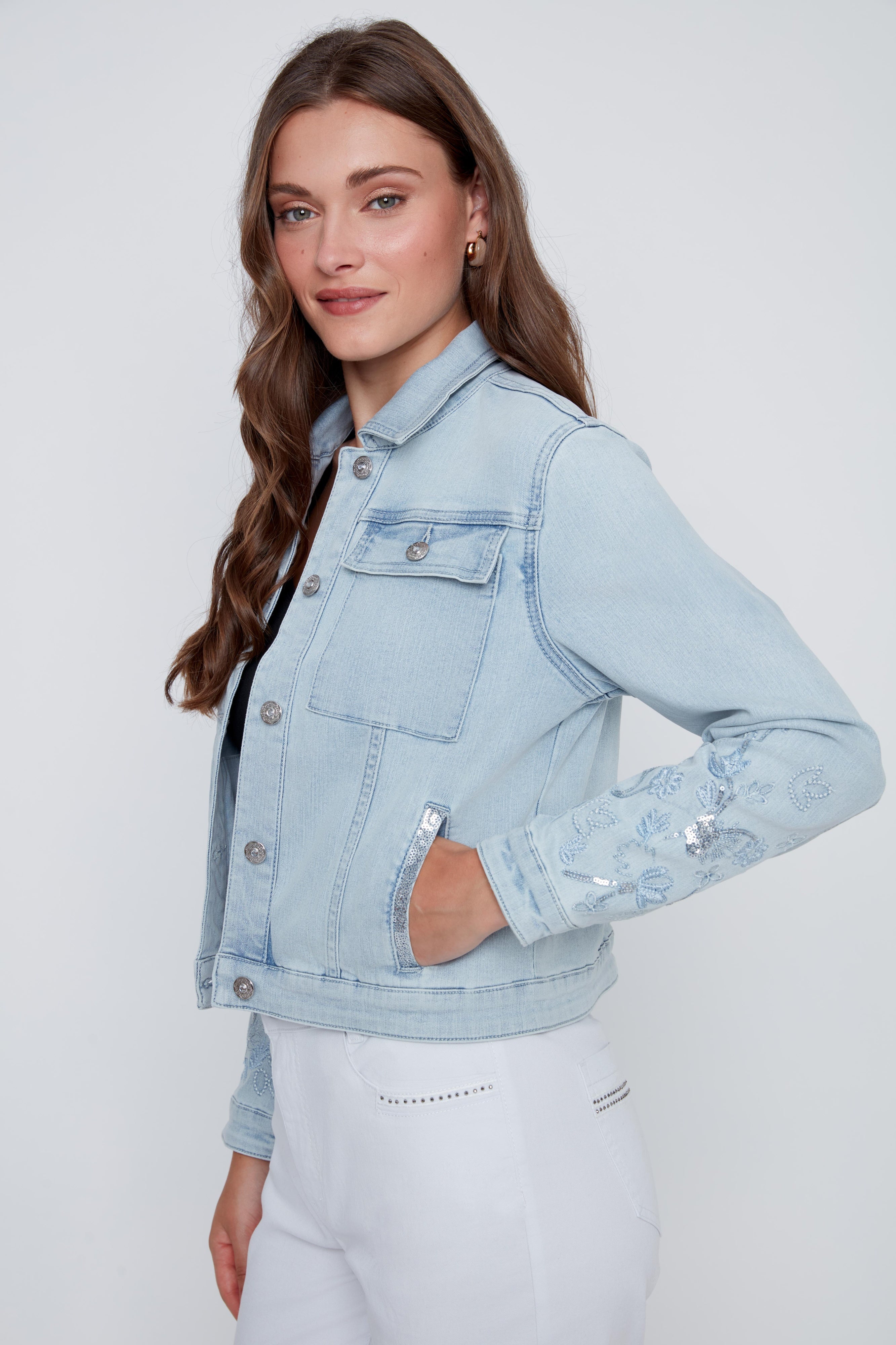 Veste de jeans pour femme en bleu denim pâle avec broderies florales à paillettes, détails brillants aux poches et boutons de fermeture à l’avant.