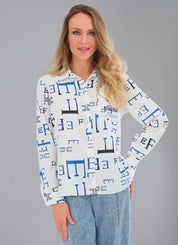 Blouse blanche fluide infroissable avec imprimé de lettres bleues, bouton nacré en forme de fleur et détails de strass sur la poche avant.
